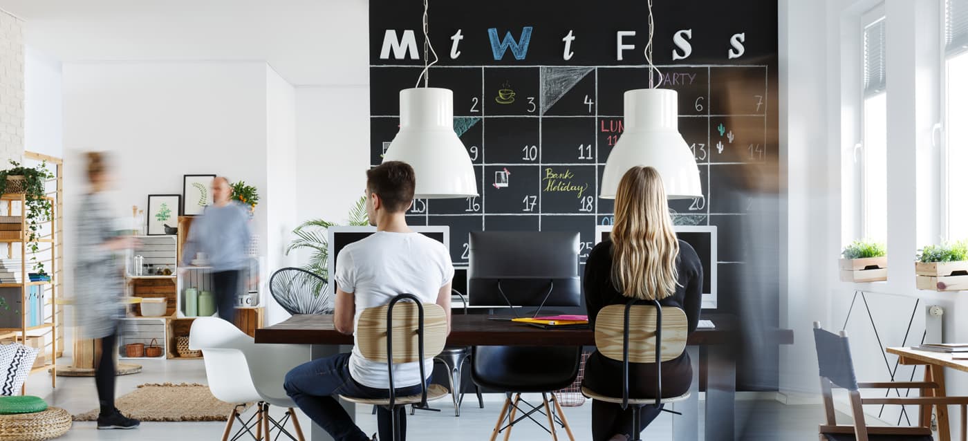 Fotografia d'un espai de coworking amb taules compartides i una pissarra tipus calendari