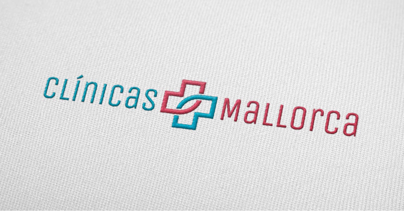 Clínicas Mallorca logo embroidered in blue and coral on white fabric