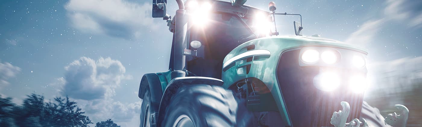 Photograph of a green tractor driving at night with its headlights on