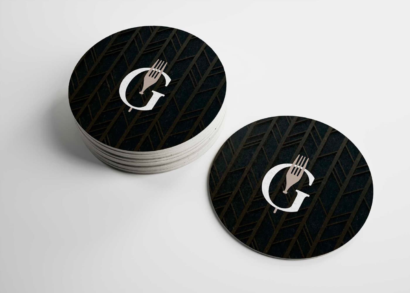 Round black coasters with the Gastrodinàmica G-and-fork icon