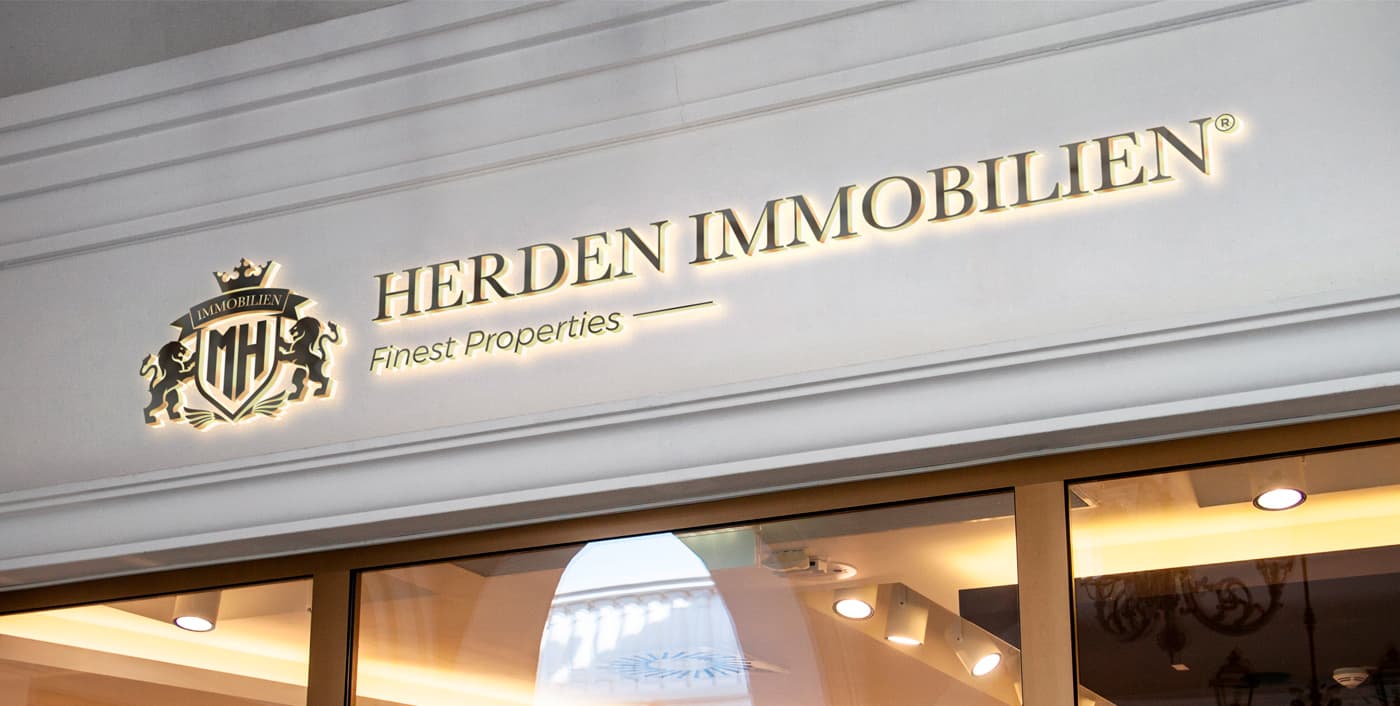 Rètol il·luminat de Herden Immobilien a la façana de l'oficina immobiliària