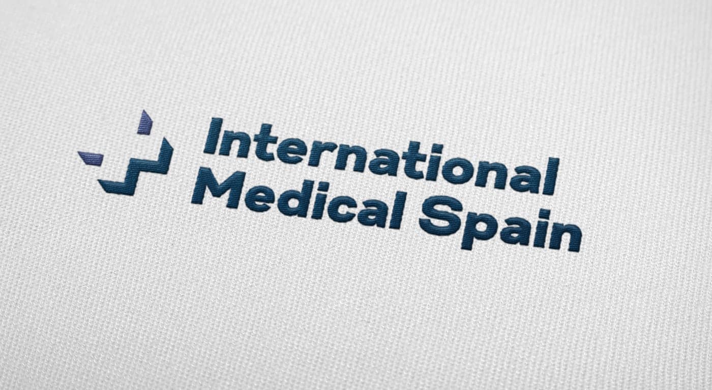 Bordado del logotipo en azul marino y morado sobre tela blanca a modo de aplicación textil