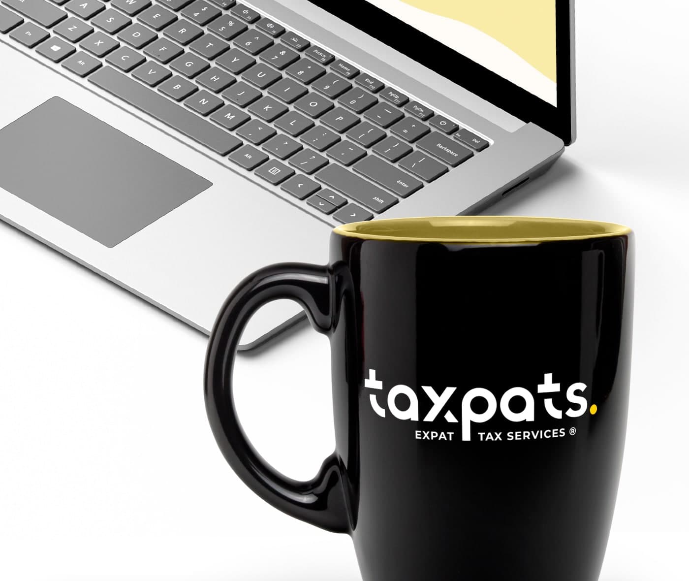Taza negra con el logotipo Taxpats junto a un ordenador portátil