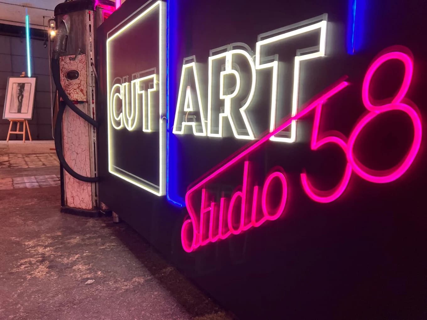 Rótulo de neón CUT ART Studio 58 encendido en el local, junto a un surtidor antiguo