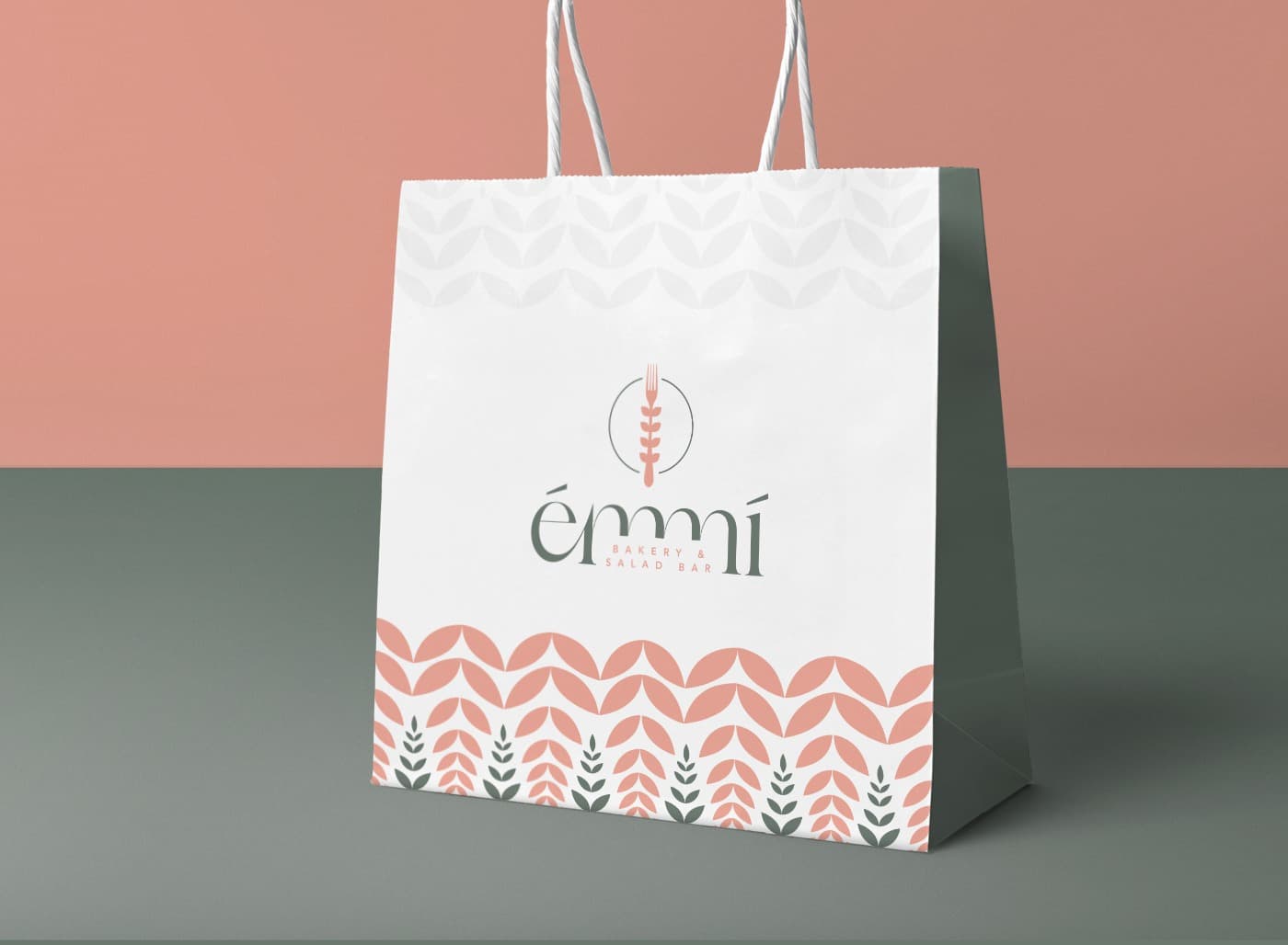 Bolsa de papel blanca con el logotipo de Émmí y estampado de hojas en coral y verde