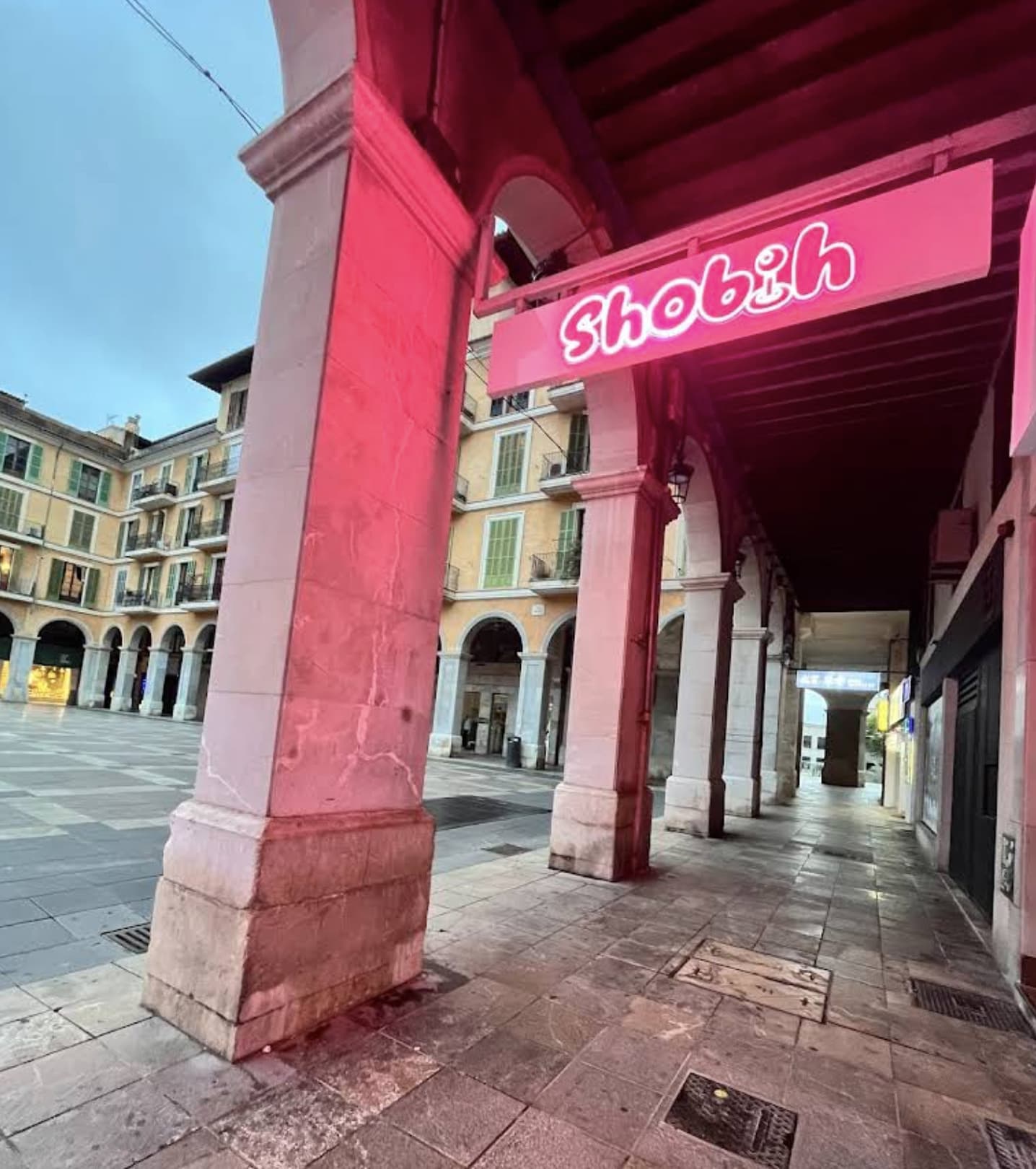 Pink neon sign of Shobih under the arches of a historic square