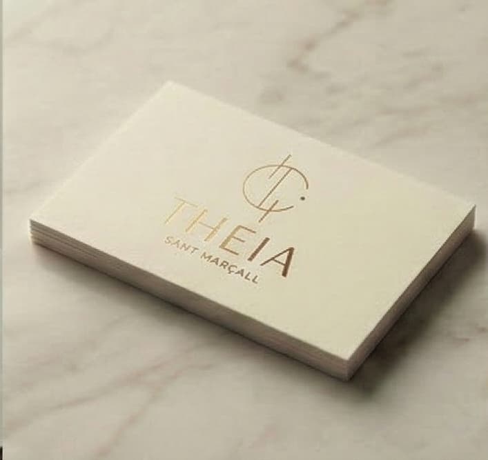 Business card with the Theia logotype stamped in gold on cream paper